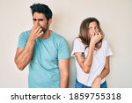 Small photo of Beautiful young couple of boyfriend and girlfriend together smelling something stinky and disgusting, intolerable smell, holding breath with fingers on nose. bad smell