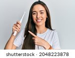 Young hispanic girl holding electric toothbrush smiling happy pointing with hand and finger 