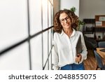 Small photo of Middle age hispanic woman smiling confident holding clipboard at office