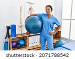 Small photo of Young african american woman wearing physio therapist uniform holding fit ball at clinic