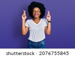 Small photo of Young african american woman wearing casual white t shirt gesturing finger crossed smiling with hope and eyes closed. luck and superstitious concept.