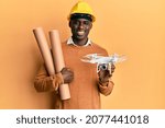 Young african american man wearing safety helmet holding blueprints and drone smiling with a happy and cool smile on face. showing teeth. 