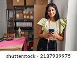 Young latin woman ecommerce business worker using smartphone at designer studio