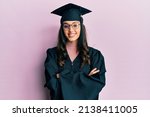 Small photo of Young hispanic woman wearing graduation cap and ceremony robe happy face smiling with crossed arms looking at the camera. positive person.