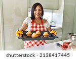 Hispanic brunette woman holding tray with homemade cupcakes at the kitchen