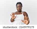 Small photo of Young african woman standing over white isolated background moving away hands palms showing refusal and denial with afraid and disgusting expression. stop and forbidden.