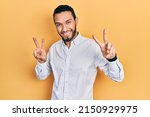 Hispanic man with beard wearing business shirt smiling looking to the camera showing fingers doing victory sign. number two. 