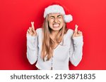 Small photo of Beautiful hispanic woman wearing christmas hat gesturing finger crossed smiling with hope and eyes closed. luck and superstitious concept.