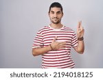 Small photo of Hispanic man with long hair standing over isolated background smiling swearing with hand on chest and fingers up, making a loyalty promise oath