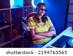 Small photo of African american woman streamer wearing thug life glasses sitting with arms crossed gesture at gaming room