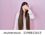 Small photo of Chinese young woman standing over pink background covering eyes with hand, looking serious and sad. sightless, hiding and rejection concept