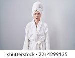 Blonde caucasian woman wearing bathrobe afraid and shocked with surprise and amazed expression, fear and excited face. 