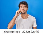 Hispanic young man standing over blue background mouth and lips shut as zip with fingers. secret and silent, taboo talking 
