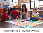 Small photo of Teacher with group of boys playing with maths puzzle game sitting on floor at kindergarten