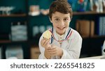 Small photo of Adorable hispanic boy student smiling confident holding gold medal at laboratory classroom
