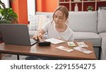 Small photo of Young blonde woman using calculator counting ruble banknotes at home