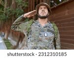 Young hispanic man wearing soldier uniform doing army salute at park