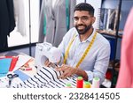 Small photo of Young arab man tailor smiling confident using sewing machine at tailor shop