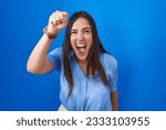 Small photo of Young brunette woman standing over blue background angry and mad raising fist frustrated and furious while shouting with anger. rage and aggressive concept.