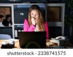 Young caucasian woman working at the office at night looking stressed and nervous with hands on mouth biting nails. anxiety problem. 