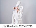 Blonde caucasian woman wearing bathrobe covering eyes with arm, looking serious and sad. sightless, hiding and rejection concept 