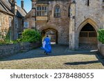 Small photo of A running clergyman with flowing robes, from behind, in ancient Vicar's Close approaching the archway that eventually leads to the Wells Cathedral, where Vespers was about to begin (without him).