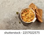 Small photo of Top view of palatable scalloped gratin potato with herbs and metal stand for hot dish near towel on gray stone surface