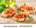 Tasty savory tomato Italian appetizers, or bruschetta, on slices of toasted baguette garnished with basil, close up on a wooden board