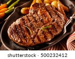 Close up view on serving of marinated grilled rib eye steak with potatoes in cast iron plate and fork