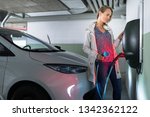 Young woman charging an electric vehicle in an underground garage equiped with e-car charger. Car sharing concept.