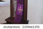 Small photo of Purple Catholic Priest Stole with Embroidered Jerusalem Cross Hanging Over Grate of Simple Church Confessional
