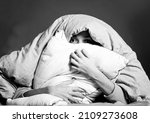 Young girl hugs a pillow, covered with a blanket from all problems. Woman worried about insomnia, poor sleep, stress panic attack and depression, creative concept in black and white.