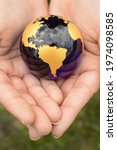 Small photo of The Earth Globe is safely held inside the palm of a womans hands overtop of a grass area.