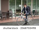 Asian businessman in a suit is riding a bicycle on the city streets for his morning commute to work. Eco Transportation Concept	