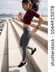 Small photo of Attractive fit female running down stairs in a midriff sport shirt with grey tights