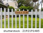 Small photo of Beware of the dog sign posted on white fence outside a house yard