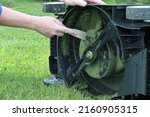 Small photo of The hand cleans the lawnmower from grass clippings. Lawn mower blade. The lower part of the lawn mower.