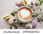 Macaroons with a cup of coffee and a branch of white flowers on a pink tile background. French dessert and flowers 