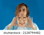 Small photo of Mental health concept. Young man holding a full-face mask, ball, or masquerade carnival mask. Symbol of bipolar disorder or hypocrisy, deceit, duplicity. Portrait of guy Prep Student with long hair