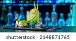 Small photo of Cocktail with cucumber, ice on bar counter in a restaurant, pub. Fresh tonic drink with lime juice, mint, gin, cucumber juice. Alcoholic cooler beverage at nightclub on dark background.