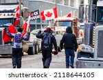 Small photo of Ottawa, Canada – February 5 2022: Supporters of the Freedom Convoy walk through a street lined with transport trucks and encourage the truckers