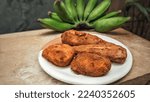 Small photo of Fried dogfish with green bananas arranged on a wooden table.