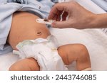 Small photo of Newborn with plastic navel clamps. Hand holding plastic navel clamps with part of dry umbilical cord.