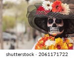 Close up of an adult woman with her eyes closed wearing La Calavera Catrina make-up and costume with a defocused background outdoors with copy space.