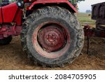 Closeup of big dirty rear wheel of tractor in paddy field. Side view of  engine area of a tractor. 