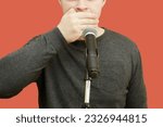 Small photo of Young man whose face cannot be seen in front of the microphone on the counter, covering his mouth with his hand. Lack of comment, reluctance to tell the truth, free speech issues