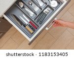 High angle top view cropped photo of woman hand open kitchen drawer by door handle, with different cutlery spoon, pizza knife, fork and stuff
