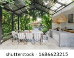 Open kitchen with empty dining room table and chairs outside, against green fresh plants on background
