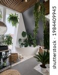 Small photo of Your own oasis at home. Cozy bathroom in urban jungle style with white freestanding tub, different tropical plants, natural wooden and wicker decor. Bath in hotel room with modern interior design
