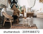 Comfortable living room with ethnic interior design in bohemian style. Apartment with home decor, rattan furniture, armchair with cushions, bamboo coffee table, carpet on wooden floor
